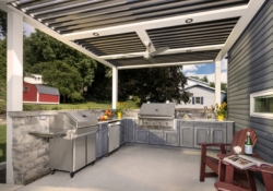 Completed Jakab outdoor kitchen with grill, sink, stone surround, pergola, and custom gray cabinetry by Mother Hubbard custom cabinetry.