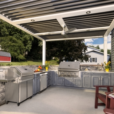 Completed Jakab outdoor kitchen with grill, sink, stone surround, pergola, and custom gray cabinetry by Mother Hubbard custom cabinetry.