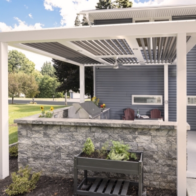 Pergola-covered Jakab outdoor kitchen with stone surround, grill, and seating by Mother Hubbard custom cabinetry.